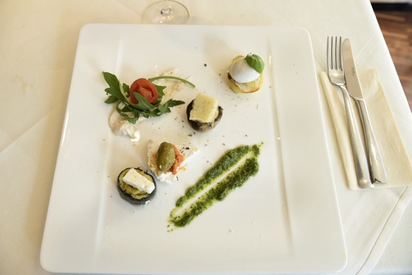 Ein elegant angerichteter Teller mit Käsehäppchen, grünem Pesto und frischem Gemüse