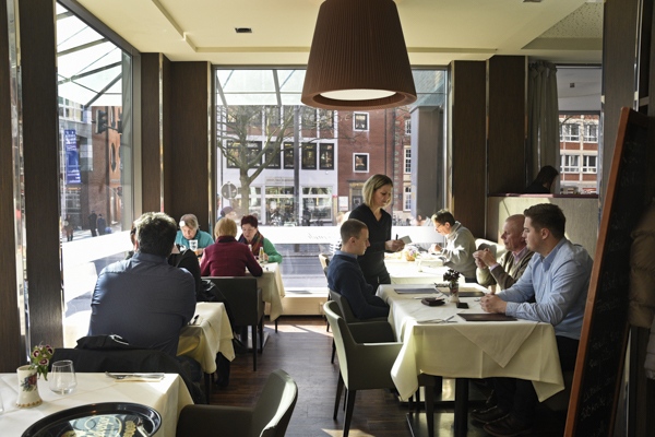 Gäste sitzen entspannt in einem modernen Café mit großem Fenster und natürlichem Licht
