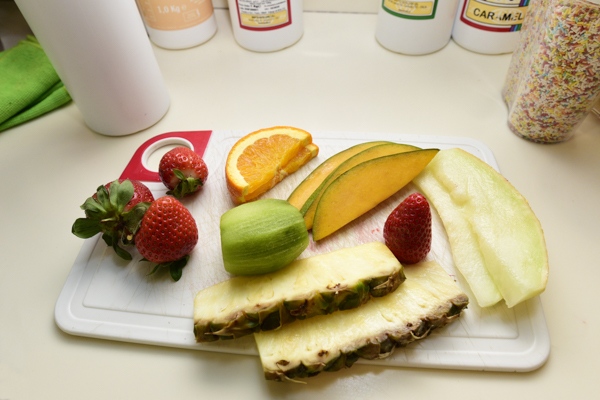 Verschiedene bunte Obstsorten wie Erdbeeren Ananas und Orange auf einem weißen Brett