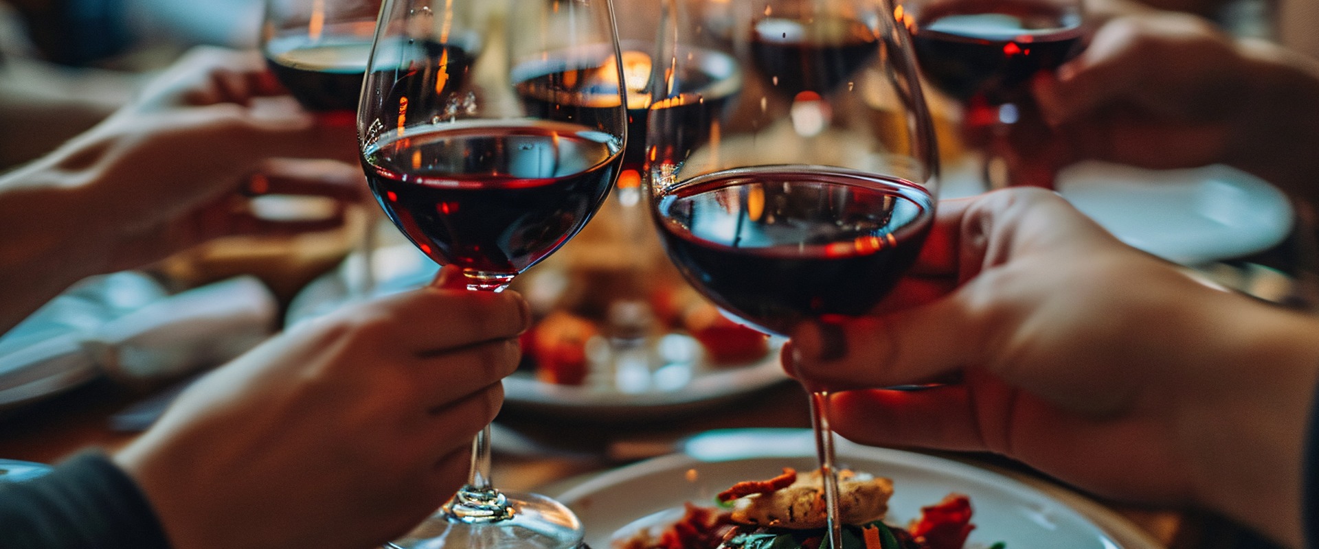 Fröhliche Gäste heben bei einem Abendessen ihre Rotweingläser. Eine Gruppe genießt ihre Mittagspause in einem Pub-Restaurant. Eine gesellige Runde mit Männern und Frauen, die sich unterhalten. Speisen und Getränke.