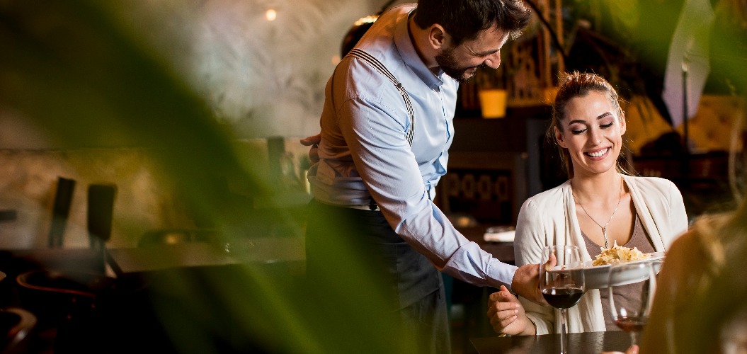 Lächelnde junge Freundinnen in einem Restaurant mit Kellner, der bedient